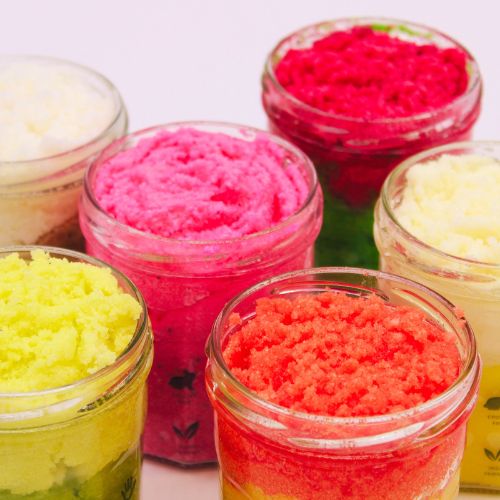 Assorted Lumaysa sugar body scrubs displayed in glass jars – colourful peach, strawberry, and citrus exfoliating scrubs arranged together.