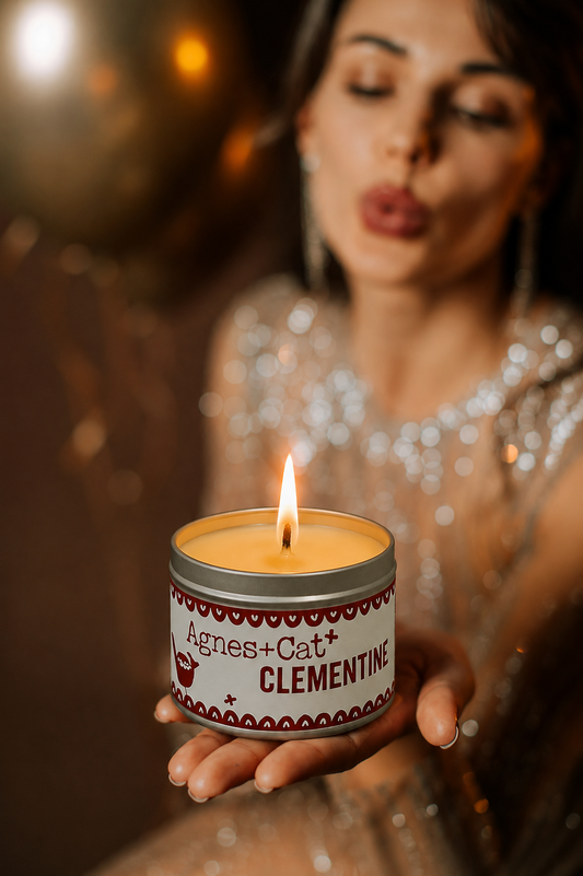 Lit Agnes + Cat Clementine soy candle held in hand, creating a warm cozy atmosphere with soft golden bokeh lights.