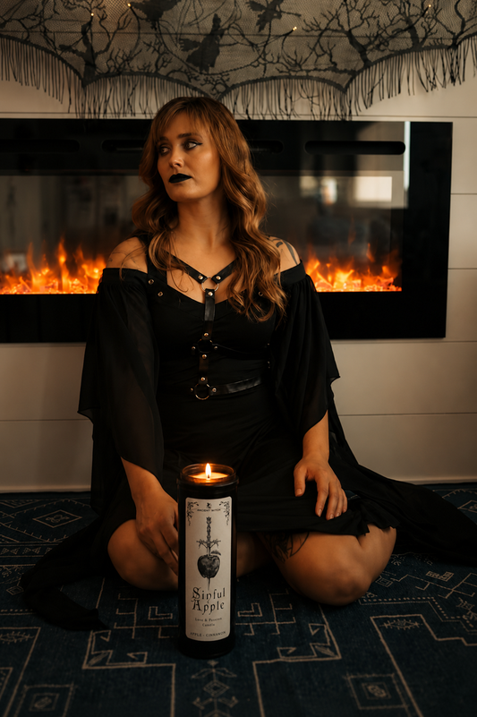 Woman in black dress holding a candle with a fireplace in the background