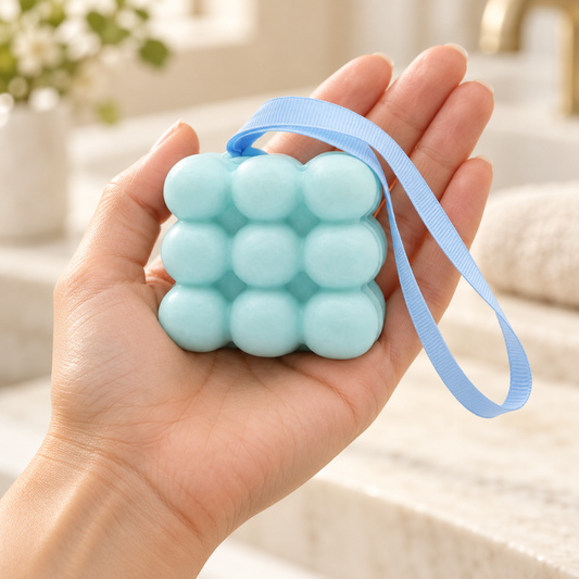 Light blue massage soap with nine rounded bumps and a blue hanging ribbon resting in an open hand to show its approximate size.