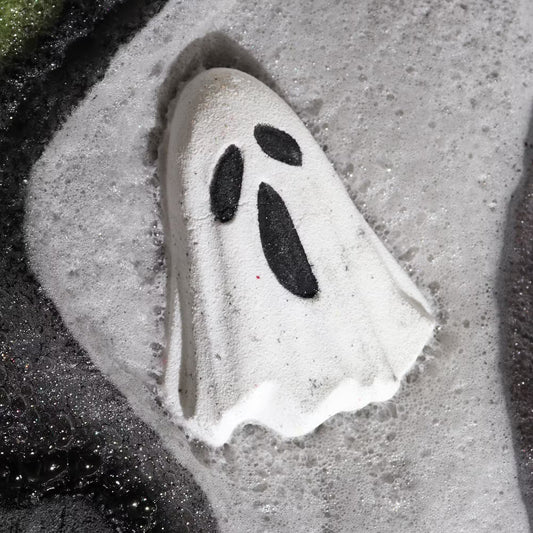 Ghost-shaped bath bomb dissolving in foamy water with dark contrast, relaxing Halloween bath ritual and spooky self-care experience