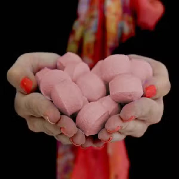 Hands holding a handful of mini passion fruit bath bomb chill pills, showing size, texture, and quantity for tropical spa baths.