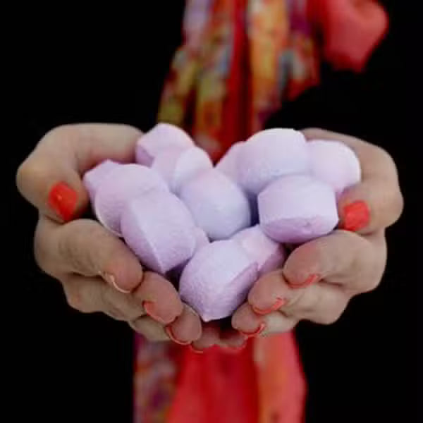 Hands holding a handful of mini black cherry bath bomb chill pills, showing size, texture, and quantity for fruity spa rituals.