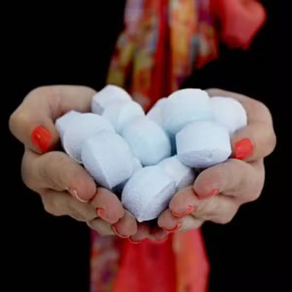 Hands holding a handful of mini lavender bath bomb chill pills, showcasing size, texture, and quantity for relaxing bath rituals.