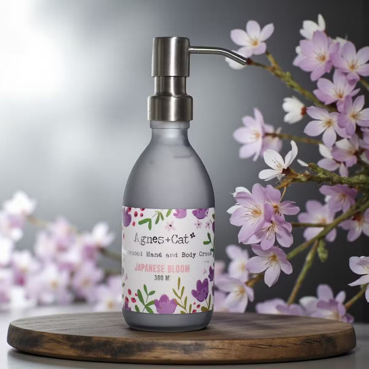 Lumaysa Sakura Whisper Hand & Body Lotion 300ml in a matte grey pump bottle, styled with soft pink sakura blossoms for an elegant floral skincare aesthetic