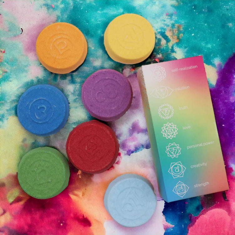 Colourful chakra bath fizzers displayed on a vibrant artistic background with a rainbow gift box, highlighting a playful and uplifting aromatherapy bath experience.
