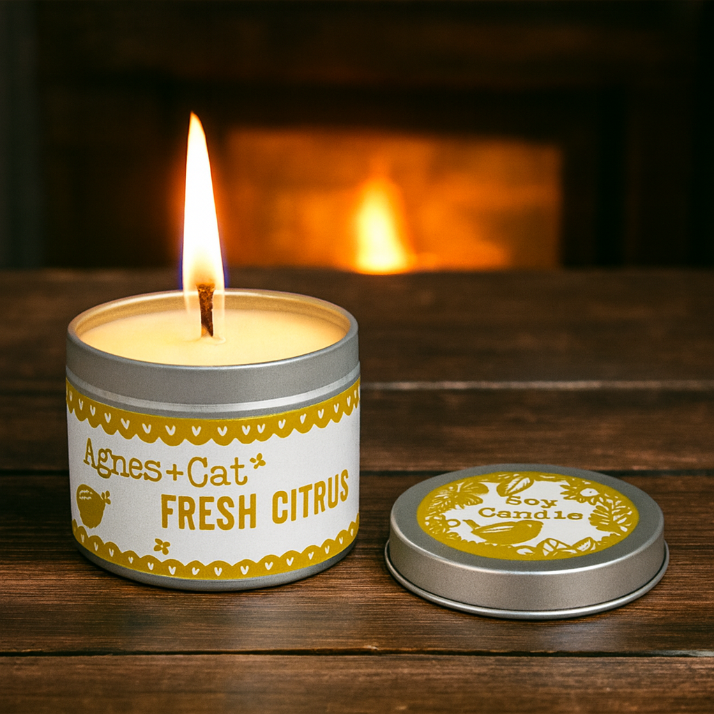 Lit Lumaysa Citrus Glow soy candle in a reusable tin with a warm cozy background and fresh citrus scent atmosphere
