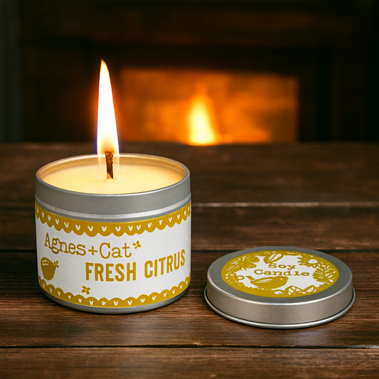 Lit Lumaysa Citrus Glow soy candle in a reusable tin with a warm cozy background and fresh citrus scent atmosphere
