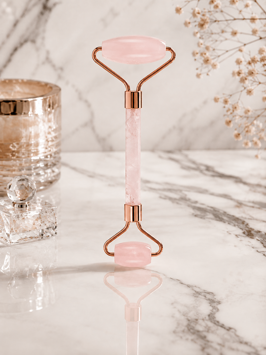 Pink and rose gold facial roller on a marble surface with decorative elements.