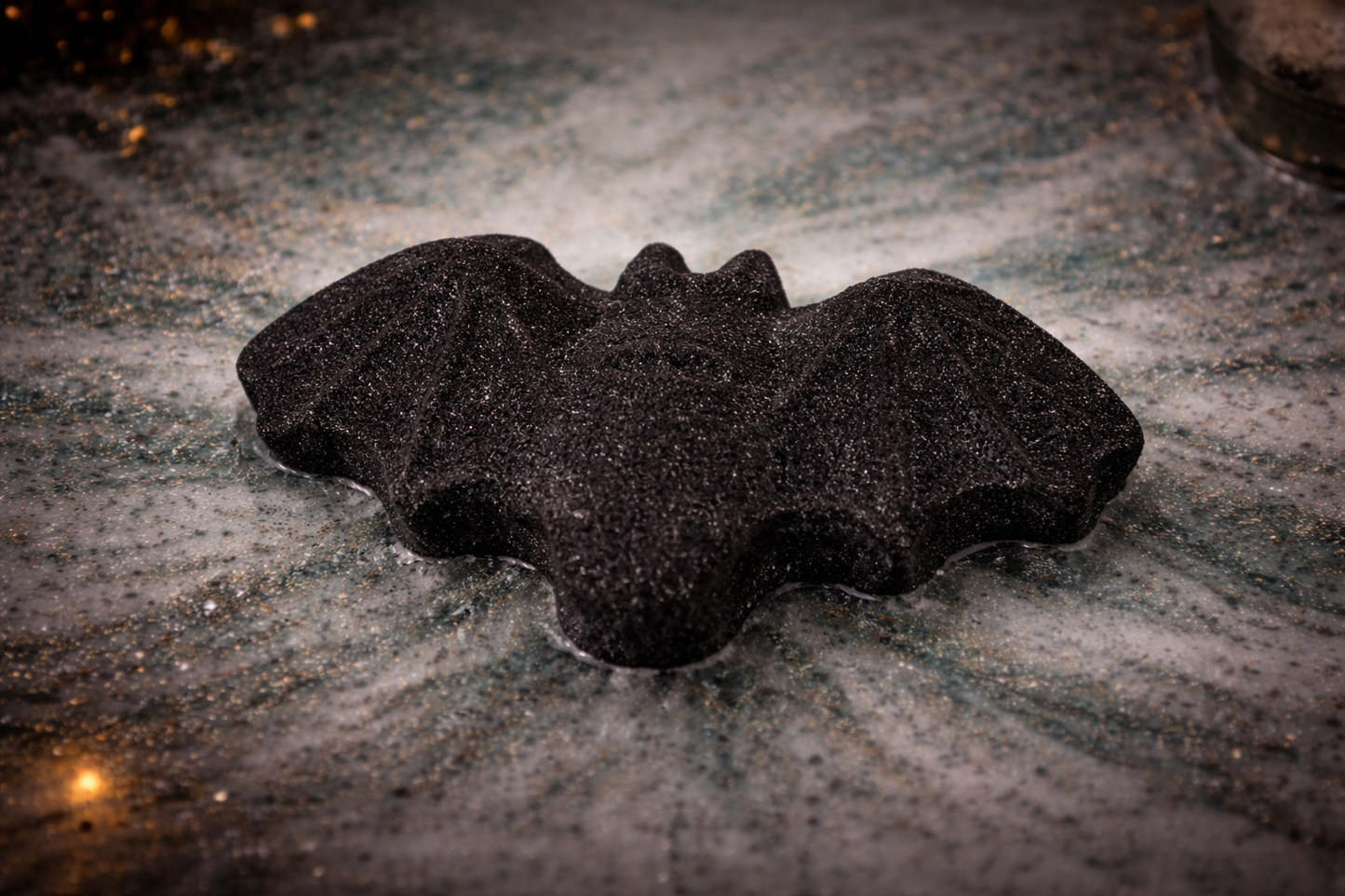 Black bat bath bomb dissolving in water, creating moody colours, a luxury Halloween bath experience by Lumaysa