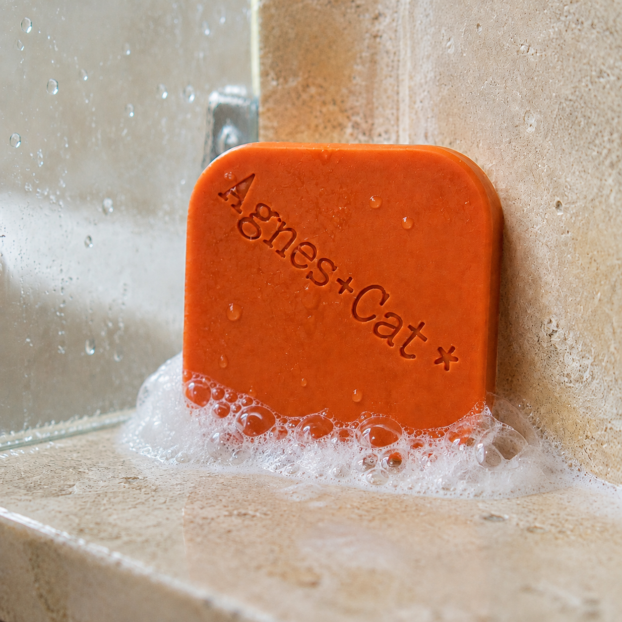 Clementine solid shampoo bar with natural foam and water droplets in a stone shower
