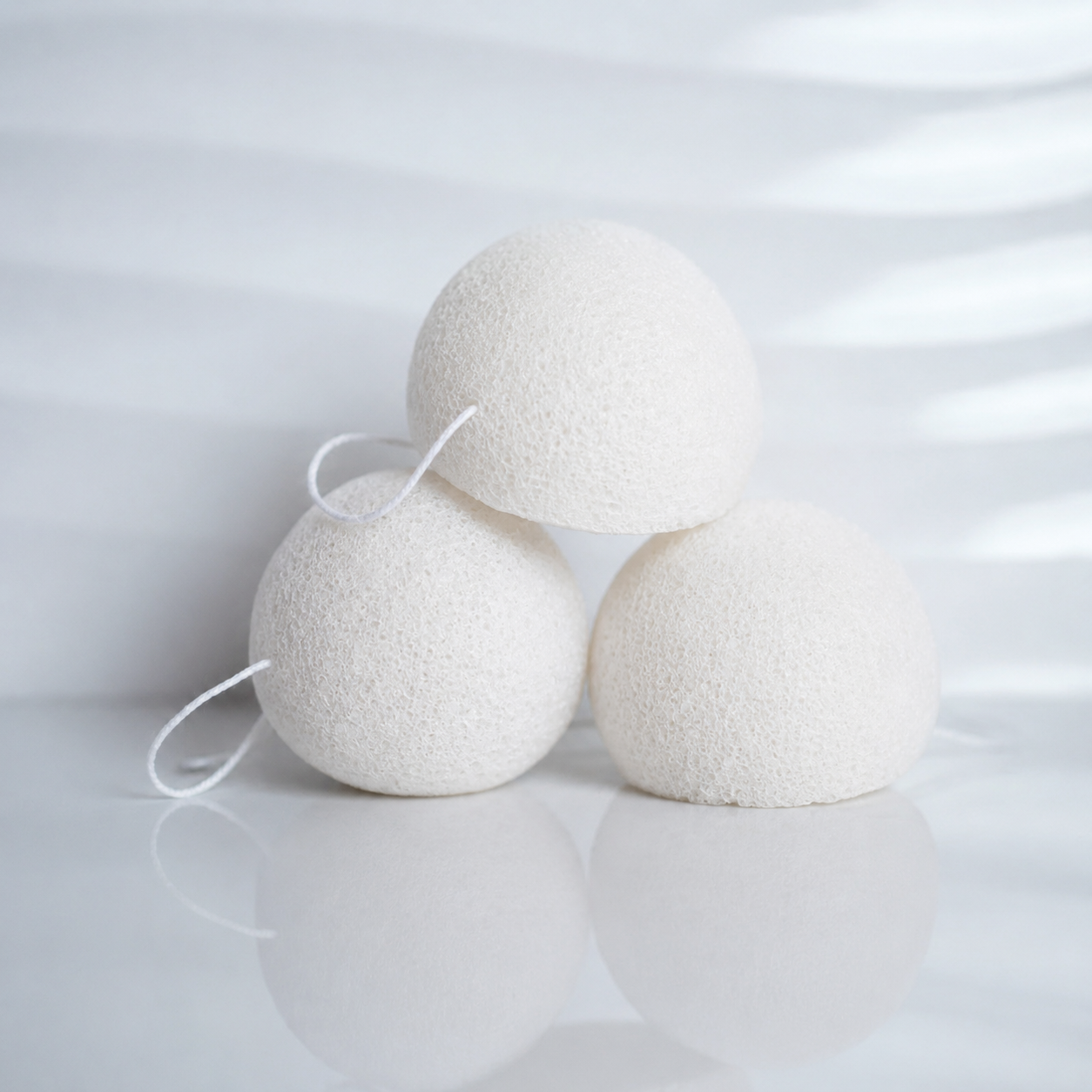 White konjac facial sponges for gentle face cleansing, stacked on a light reflective background