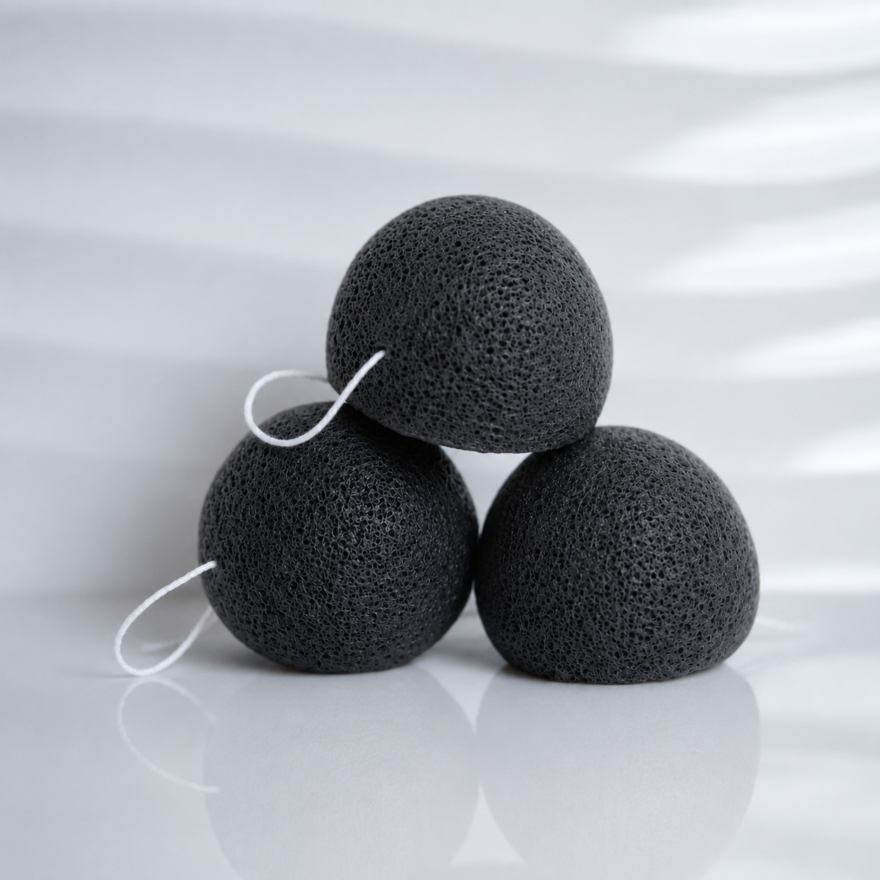 Three black bamboo charcoal konjac sponges with white hanging strings on a clean white background.
