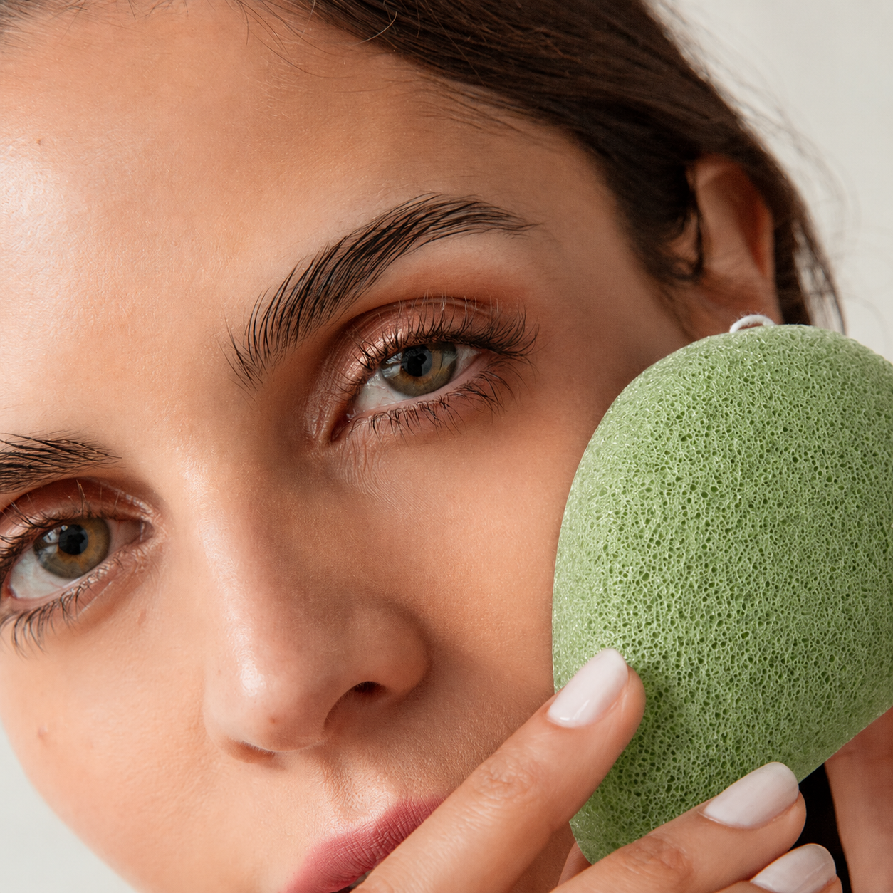 Woman gently cleansing her face with an antioxidant green tea konjac sponge.