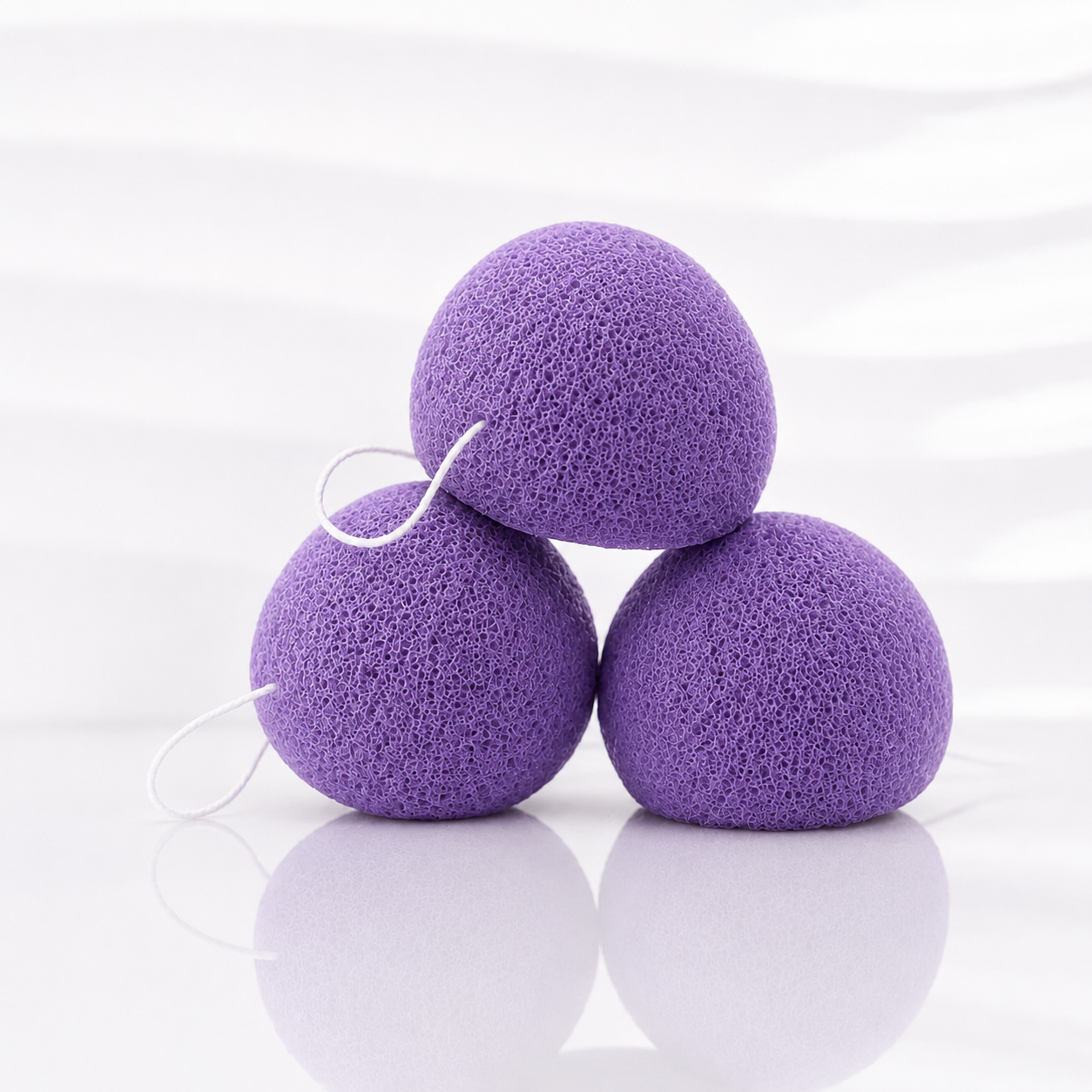 Three lavender konjac facial sponges with white hanging strings on a clean white background.