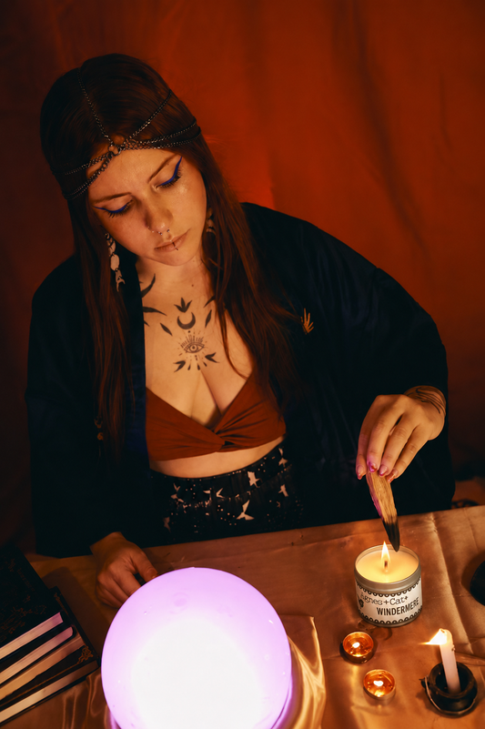 Woman performing a ritual with candles and a crystal ball in a dimly lit room.