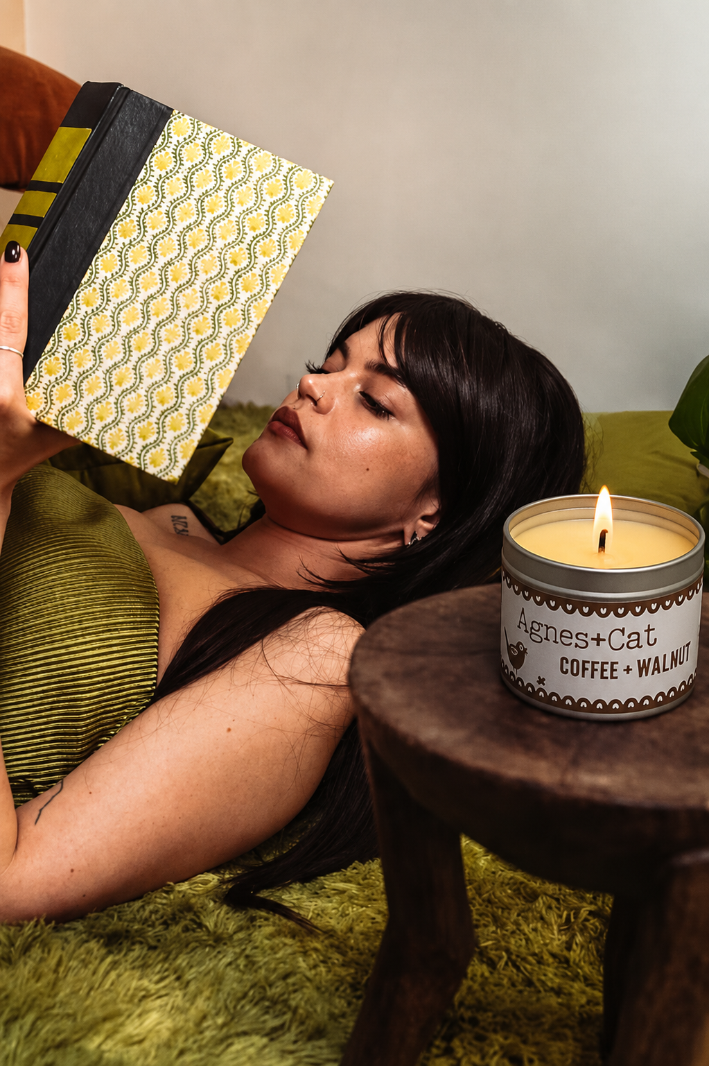 Woman lying on a green couch with a patterned box and a lit candle on a wooden table.