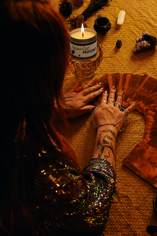 Person with tattooed hands performing a ritual with a candle and crystals on a yellow surface