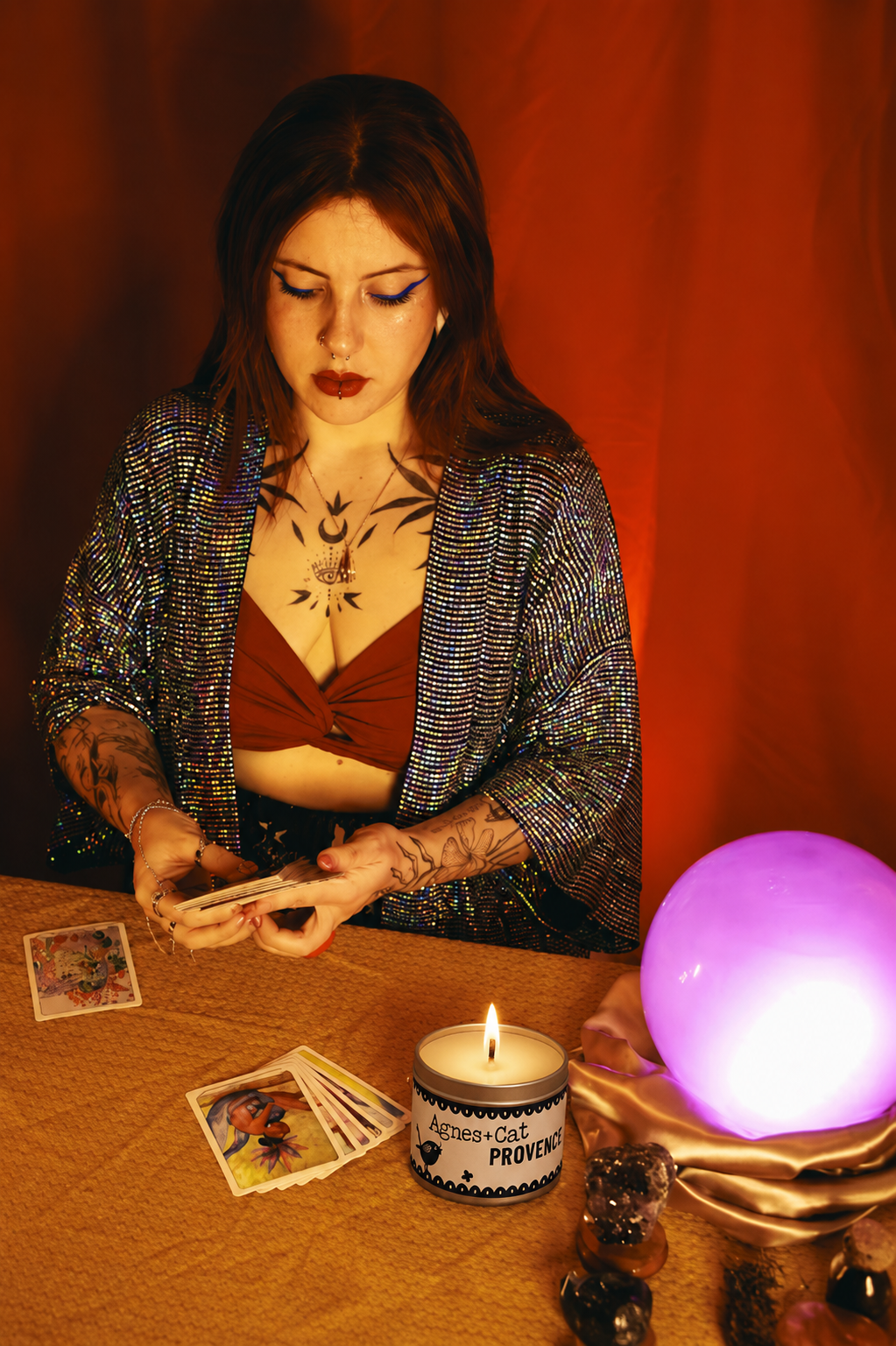 Woman in a mystical setting with tarot cards, candle, and crystal ball against a red curtain.