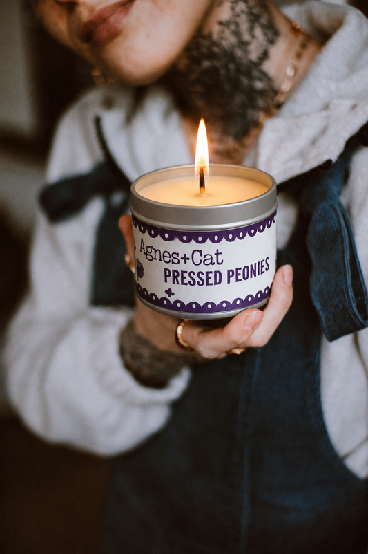 Person holding a lit candle in a 'Agnes + Cat Pressed Peonies' tin
