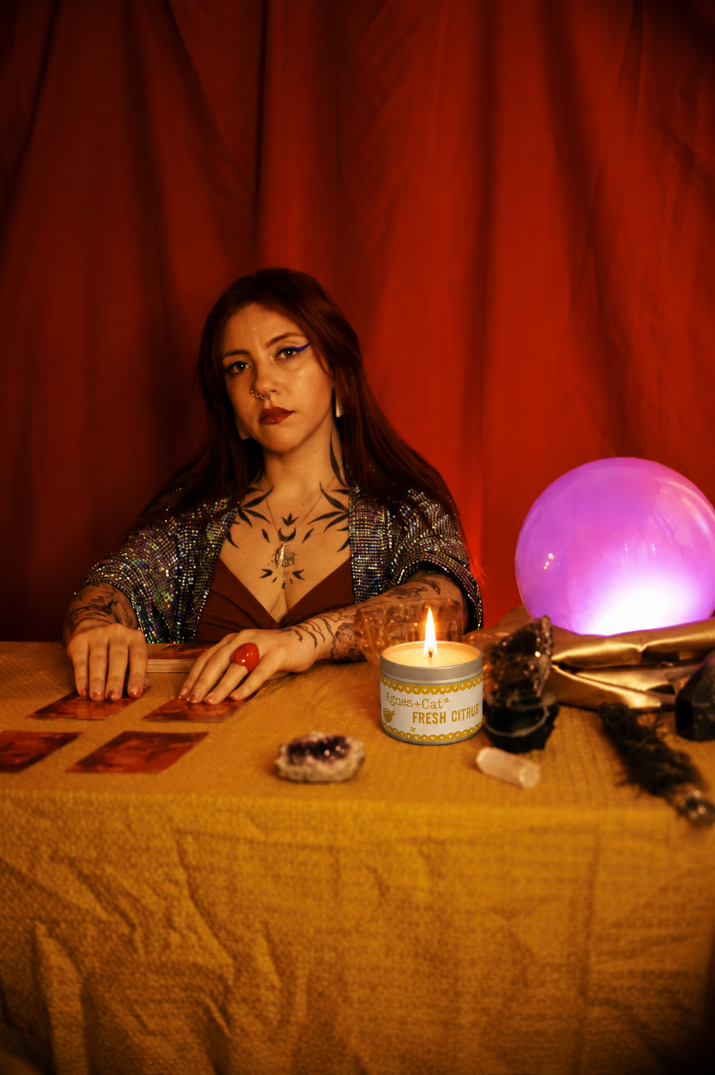 Woman at a tarot reading setup with a candle, tarot cards, and a crystal ball on a red curtain background.