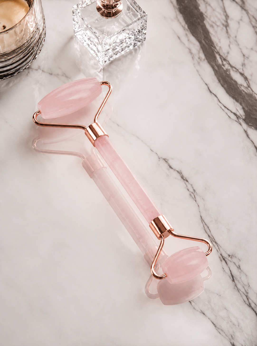 Pink facial roller with rose gold accents on a marble surface