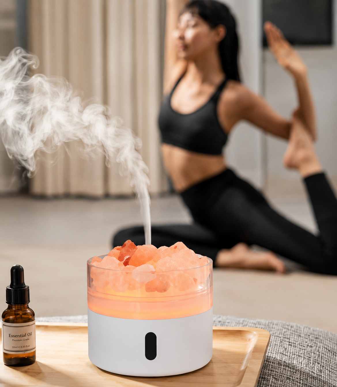 Person practicing yoga with a diffuser and essential oil bottle on a wooden table.