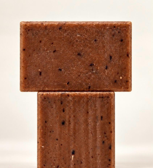 Two brown lavender and vanilla soap bars stacked in a T shape against a cream background, showing their textured surfaces and botanical flecks.