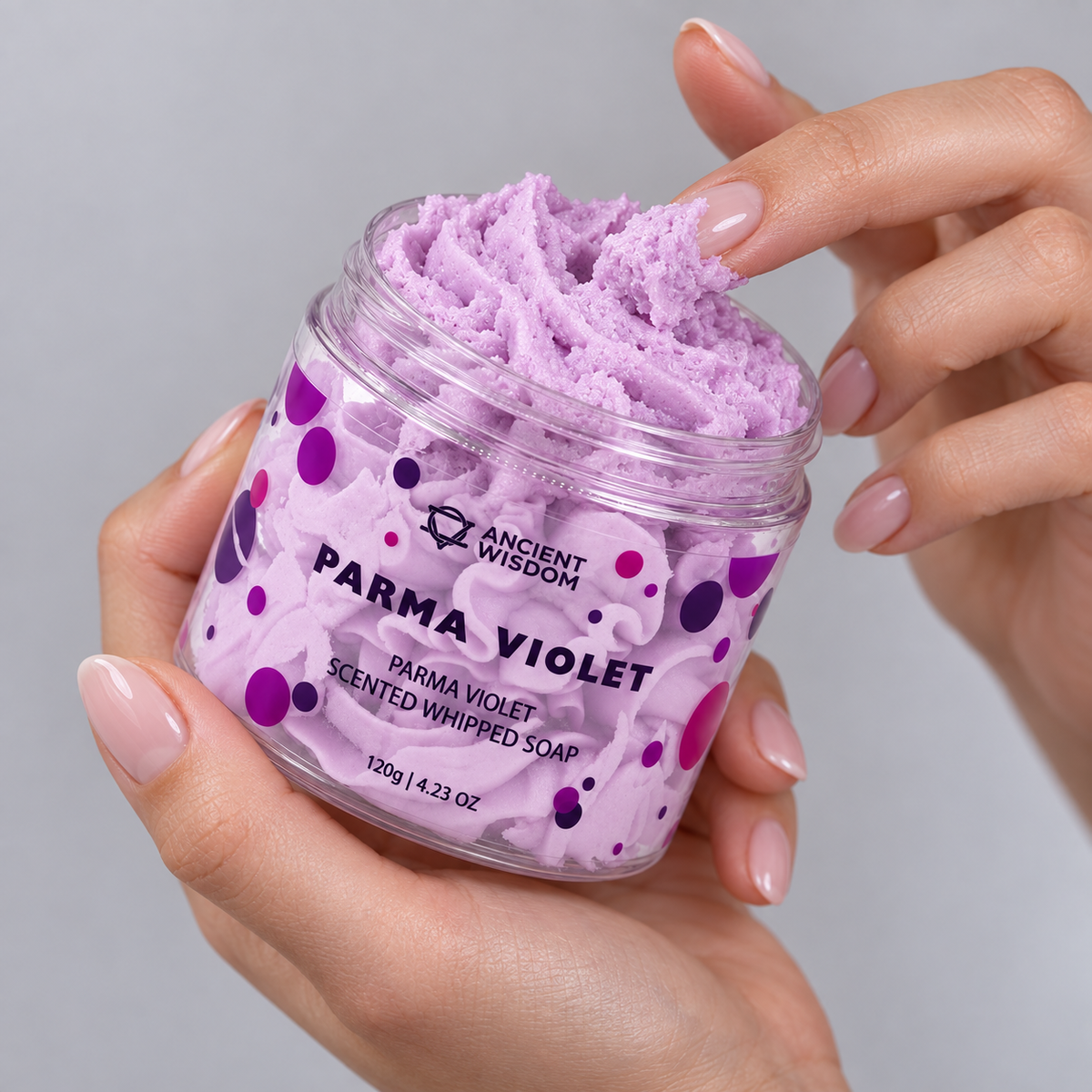 Hands holding an open jar of Parma Violet Scented Whipped Soap 120g and touching its soft lilac texture