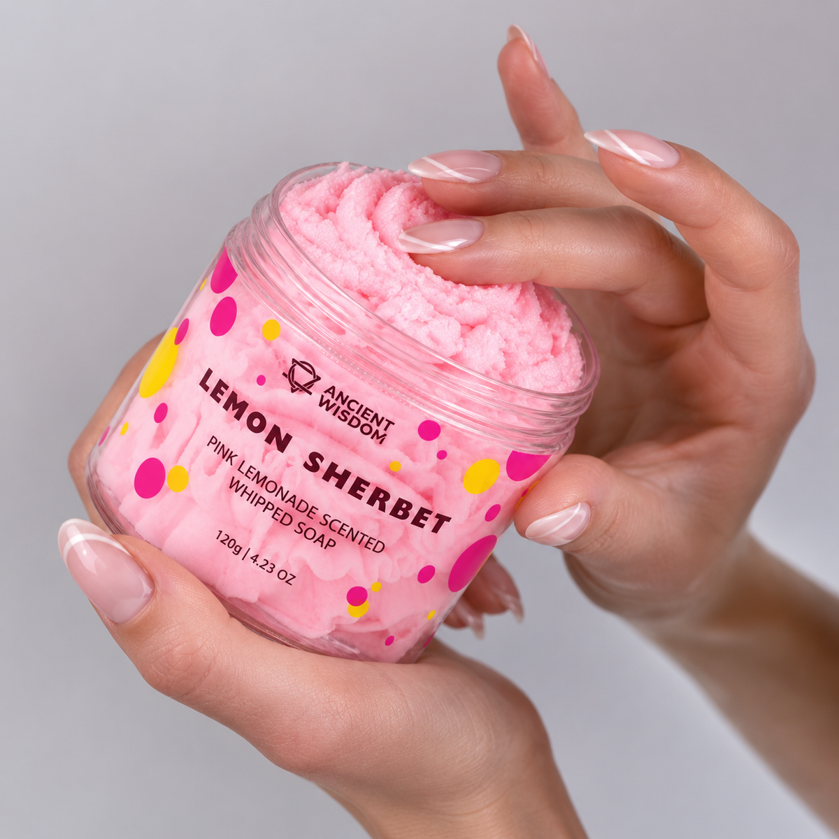 Hands holding an open jar of soft pink Lemon Sherbet and gently touching its creamy whipped-soap texture.
