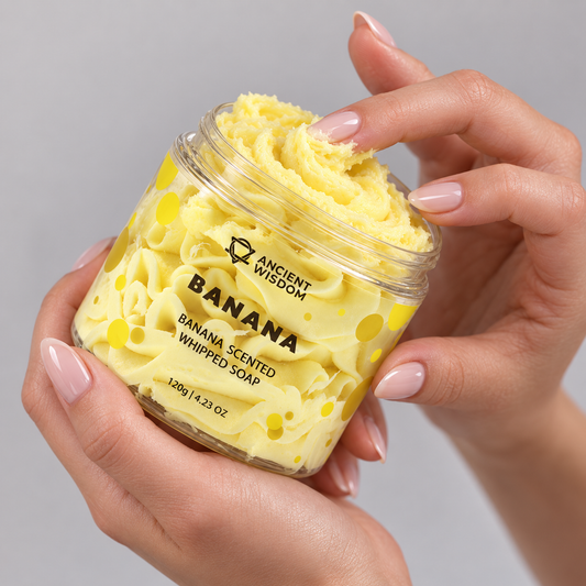 Hands holding an open jar of Banana Scented Whipped Soap 120g and touching its creamy yellow texture