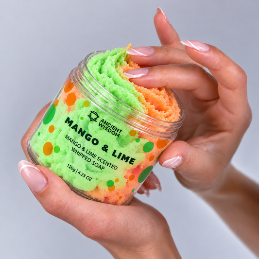 Woman holding an open jar of two-tone green and orange Mango & Lime Whipped Soap while gently touching its creamy texture.