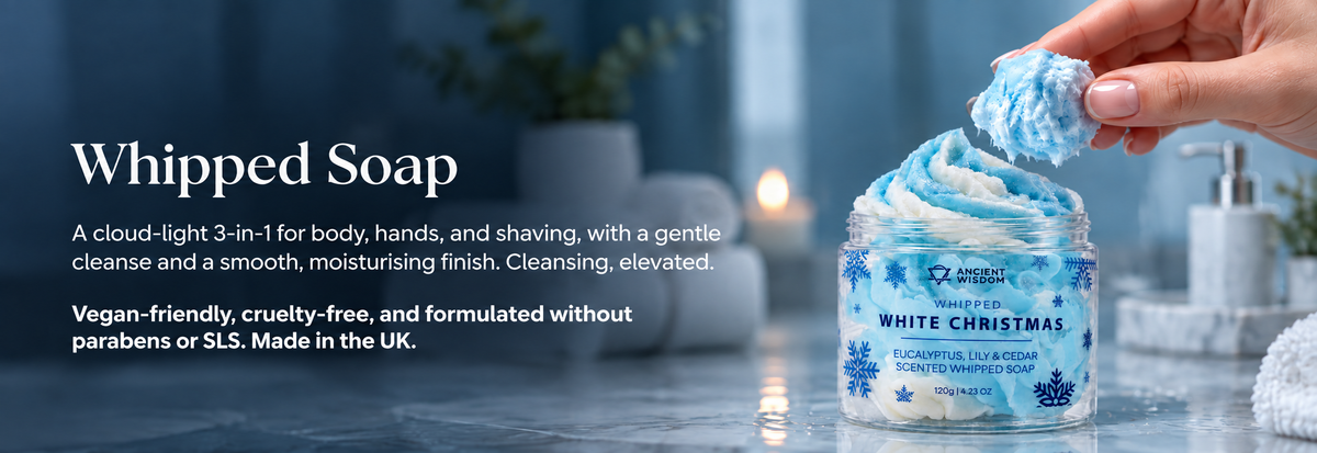 Blue and white Whipped White Christmas soap in a clear jar, with a hand lifting its cloud-like texture in a luxurious spa setting.