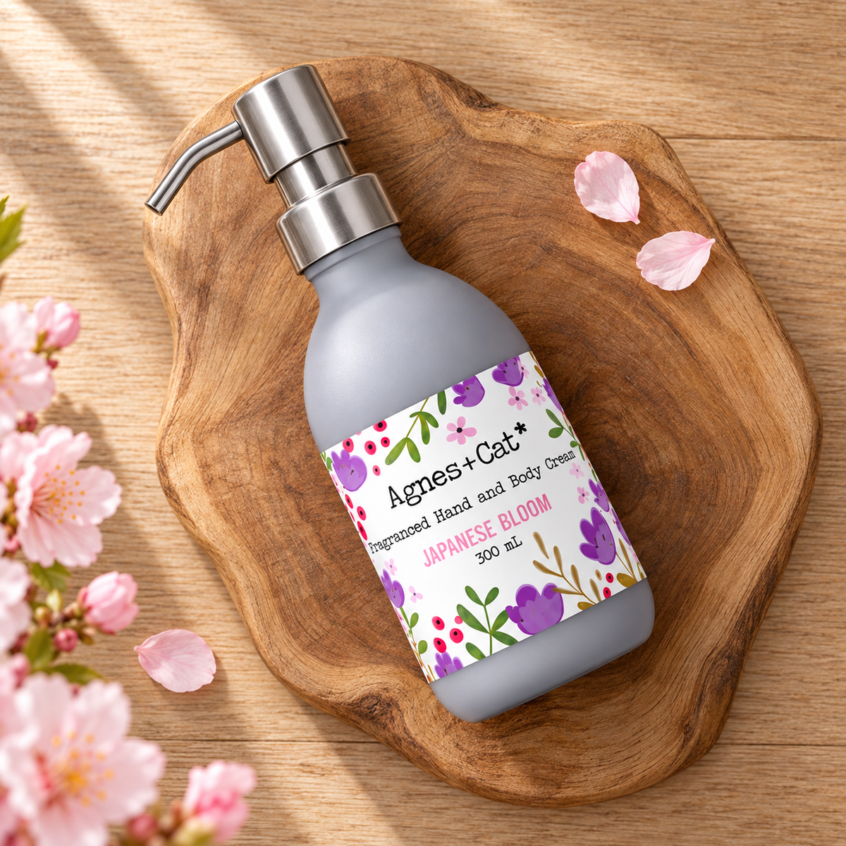 Agnes + Cat Japanese Bloom Hand and Body Cream 300ml arranged on a natural wooden board with soft pink cherry blossom petals