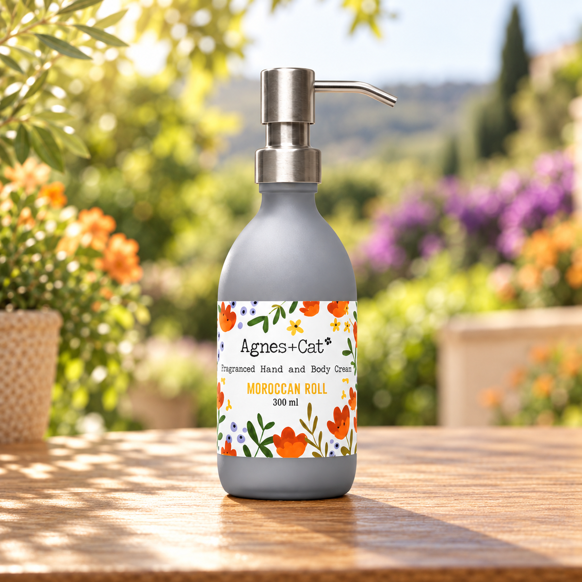 Agnes + Cat Moroccan Roll Hand and Body Cream 300ml displayed on a wooden table in a sunlit flower garden