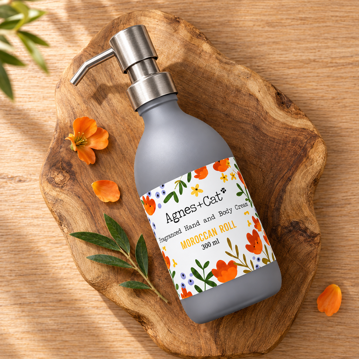 Agnes + Cat Moroccan Roll Hand and Body Cream 300ml arranged on a natural wooden board with orange flowers and green leaves