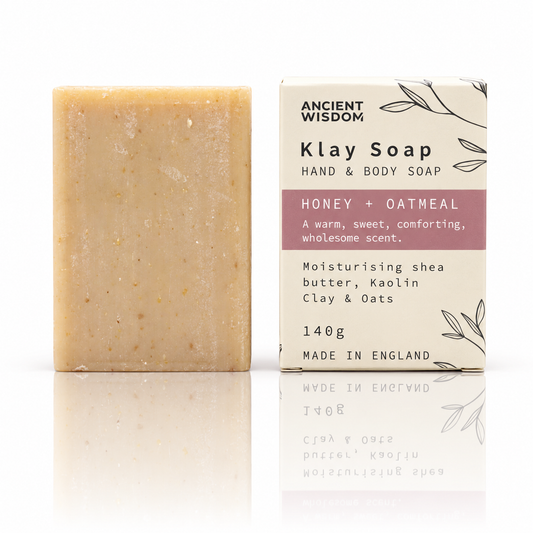 Honey and oatmeal Klay Soap bar beside its Ancient Wisdom packaging on a white background with a soft reflection.