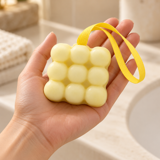 Pale yellow massage soap with nine rounded bumps and a yellow hanging ribbon resting in an open hand to show its approximate size.