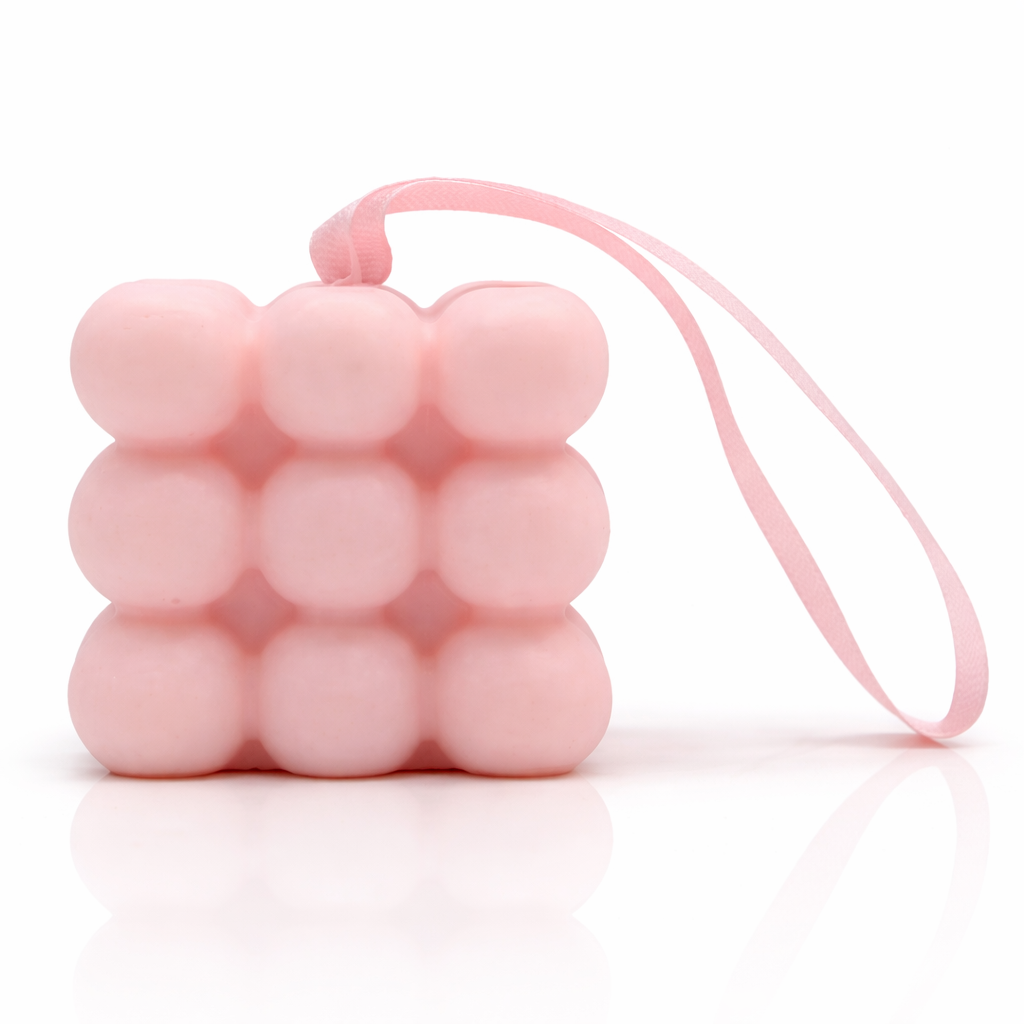 Pink bubble massage soap with hanging ribbon, clean white background with soft reflection, premium spa skincare product photography
