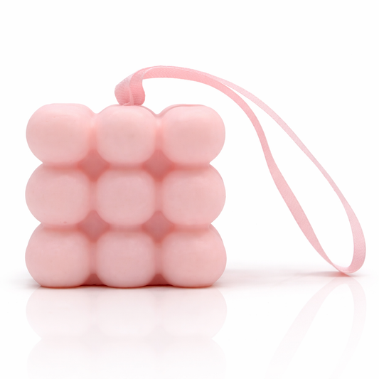 Pink bubble massage soap with hanging ribbon, clean white background with soft reflection, premium spa skincare product photography