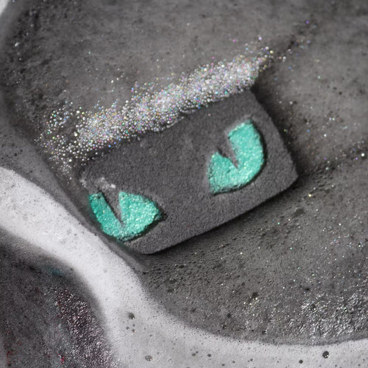 Cat eyes bath bomb dissolving in dark water with foam and shimmer, spooky Halloween bath experience with glowing effect