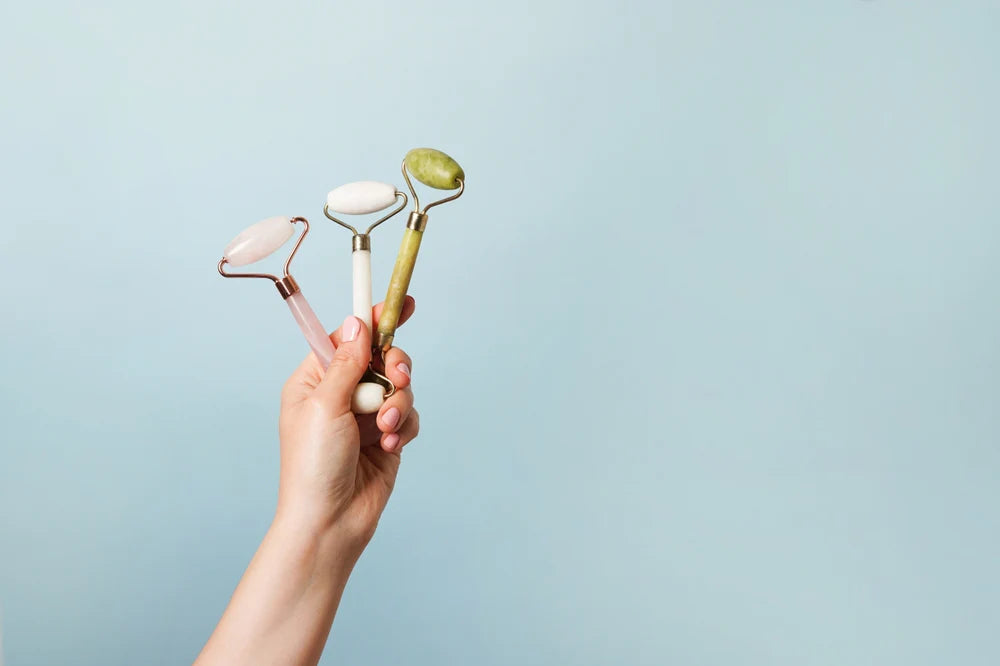 Hand holding three skincare tools against a light blue background