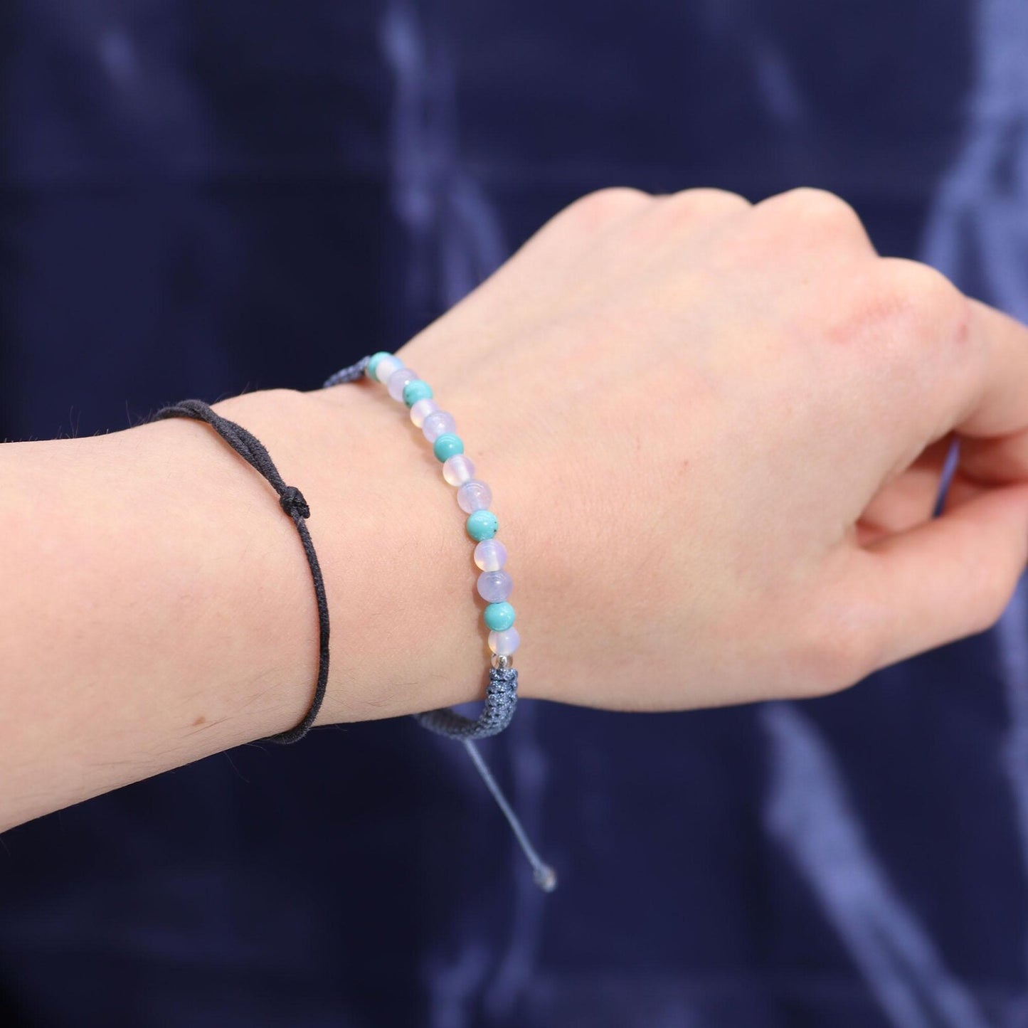 Hand wearing a Pisces-inspired beaded bracelet with soft blue and purple stones against a dark background.