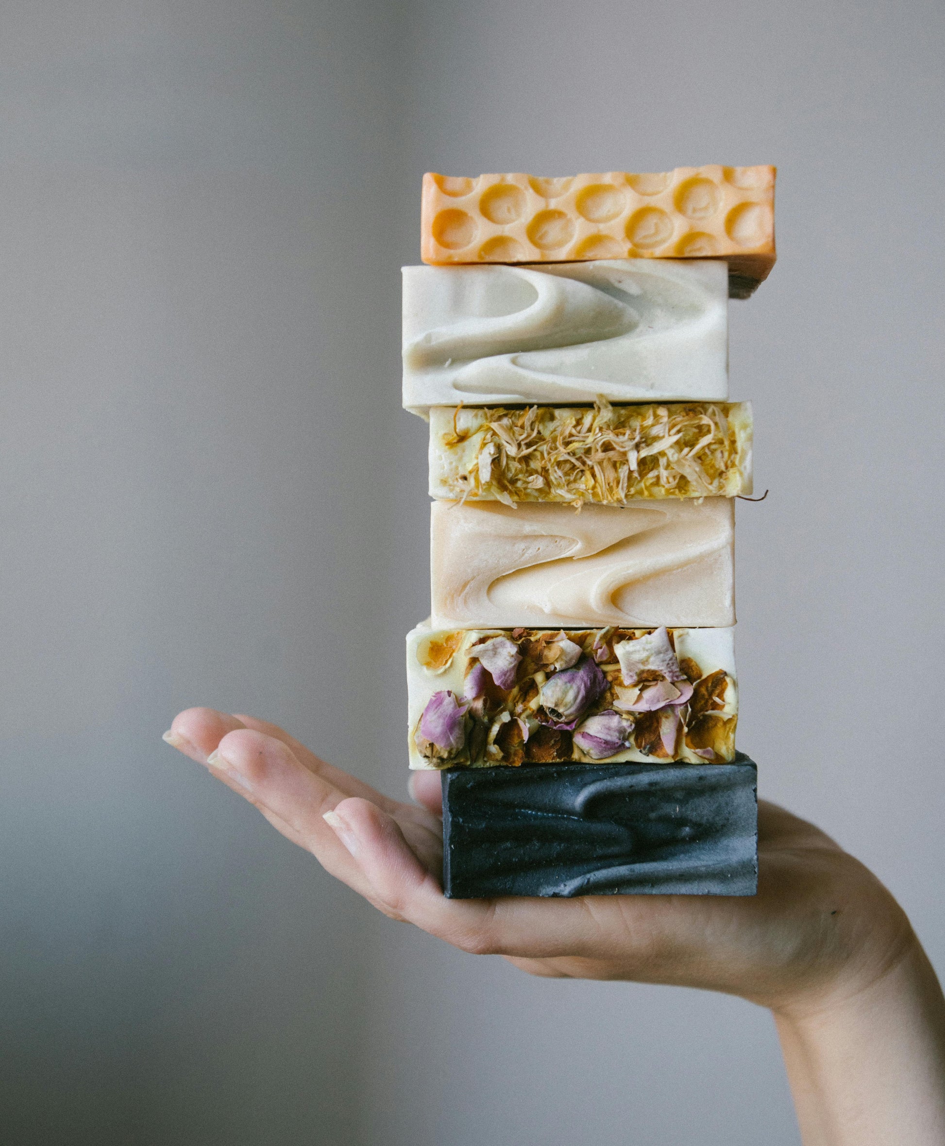 Stack of various soap bars held in a hand against a neutral background