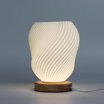 Lumaysa Shell Flow sculpted ambient table lamp with flowing shell-inspired design and natural wooden base, emitting a soft warm glow