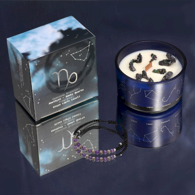 Lumaysa Zodiac Harmony Capricorn Crystal Soy Candle with Amethyst & Smoky Quartz bracelet displayed in glass jar with constellation box on a reflective surface 